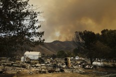 The remains of mobile homes devastated by a wildfire are seen in the foreground as smoke rises over a mountain, Saturday, June 25, 2016, in South Lake, Calif. AP Photo/Jae C. Hong

