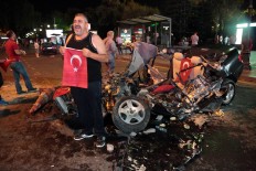 A man poses with the flag of Turkey in front of a damaged car, crashed by a military tank as people gather in Kizilay Square to protest against a military coup in Ankara, Turkey, early Saturday, July 16, 2016. Turkish President Recep Tayyip Erdogan told the nation Saturday that his government was working to crush a coup attempt after a night of explosions, air battles and gunfire across the capital. AP Photo/Burhan Ozbilici