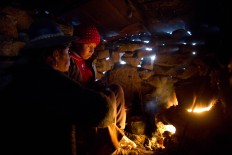In this July 9, 2016 photo, Rosa Carcabusto and her daughter Maria Luque warm themselves by the fire where they cook soup made of wheat and dried potatoes in San Antonio de Putina in the Puno region of Peru. In stark contrast to the high prices charged by designer brands for alpaca wool goods is the daily struggle against the elements and poverty by the thousands of highland shepherds whose livelihood depends on the trade. AP Photo/Rodrigo Abd