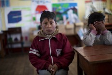 In this July 9, 2016 photo, a student waits for class to start at his public school in San Antonio de Putina in the Puno region of Peru. Due to the recent sub-freezing temperatures, the start of the school day has been delayed to 9am. AP Photo/Rodrigo Abd