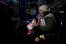 In this July 11, 2016 photo, Ruth Aguilar holds her daughter Chaska, which translates as "Star" in the Quechua language, as a doctor inspects the baby suffering a respiratory infection in San Antonio de Putina in the Puno region of Peru. Two months into the cold season an estimated 14,000 children in the Andes have suffered from respiratory illnesses and 105 died, according to government figures. AP Photo/Rodrigo Abd