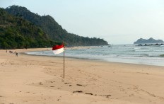 A red-and-white flag blows in the wind on a beach near the island. JP/Tarko Sudiarno