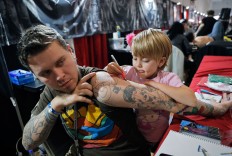 In this picture taken on Sunday, Oct. 16, 2016, Ave, 4 year-old from  the United States, paints on her father's arm during the International Tattoo Convention Bucharest 2016 in Bucharest, Romania. More than 100 tattoo and piercing artists brought their skills and art to a three-day convention in the Romanian capital. AP Photo/Vadim Ghirda