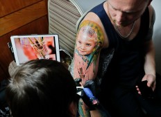 In this picture taken on Sunday, Oct. 16, 2016, Serghei, from the Republic of Moldova, gets a tattoo showing his son Chiril applied to his hand, during the International Tattoo Convention Bucharest 2016 in Bucharest, Romania. AP Photo/Vadim Ghirda
