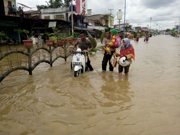 People walk through a flood on Nov. 15, 2025,  in Rokan Hulu regency in Riau. 