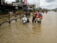 People walk through a flood on Nov. 15, 2025,  in Rokan Hulu regency in Riau. 