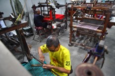 Two men work on lurik cloths using a manual weaving machine. JP/Aditya Sagita