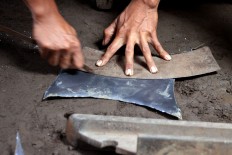 A man cuts a metal plate into a pattern for a kenong, a metal percussion set like a bonang, but bigger. JP/Aditya Sagita