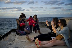 In this Jan. 30, 2017 photo, boxers Idamerys Moreno, left, and Legnis Cala, get ready for a photo session, as tourists take photos of the sunset, on Havana's sea wall in Cuba. Female athletes in Cuba have made strides in many other sports, including wrestling, judo and most recently, weightlifting, but not in boxing. AP/Ramon Espinosa