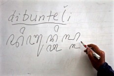 A teacher writes the word dibunteli (wrapped) in Javanese script on a white board. JP/ Aditya Sagita