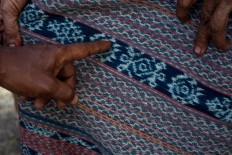 A Sikka woman points to one of the sacred symbols in the traditional ikat cloths. The motif represents women’s fertility. JP/Intan Tanjung