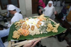 An ustadz carries a bamboo plate of rice and side dishes – comprising urap (vegetables with shredded coconut, fried tempeh and tofu, boiled egg and crackers) – to break the fast. JP/Maksum Nur Fauzan