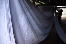 A craftsman hangs up sheets of fabric to dry the patterns applied in wax before the dyeing process. JP/Aman Rochman