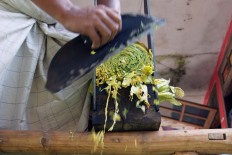 A worker uses a rudimentary blade and feeder to slice rolls of tobacco leaves into thin shreds. JP/Wahyoe Boediwardhana