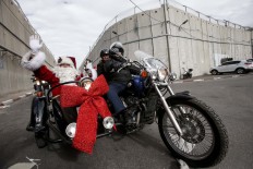 A man dressed as Santa Claus waves to people as he rides in the sidecar of a motorcycle, ahead of the motorcade of Archbishop Pierbattista Pizzaballa, Apostolic Administrator of the Latin Patriarchate of Jerusalem, while crossing through an Israeli checkpoint in the controversial separation barrier to attend Christmas eve celebrations in the West Bank city of Bethlehem December 24, 2017. AFP/Hazem Bader