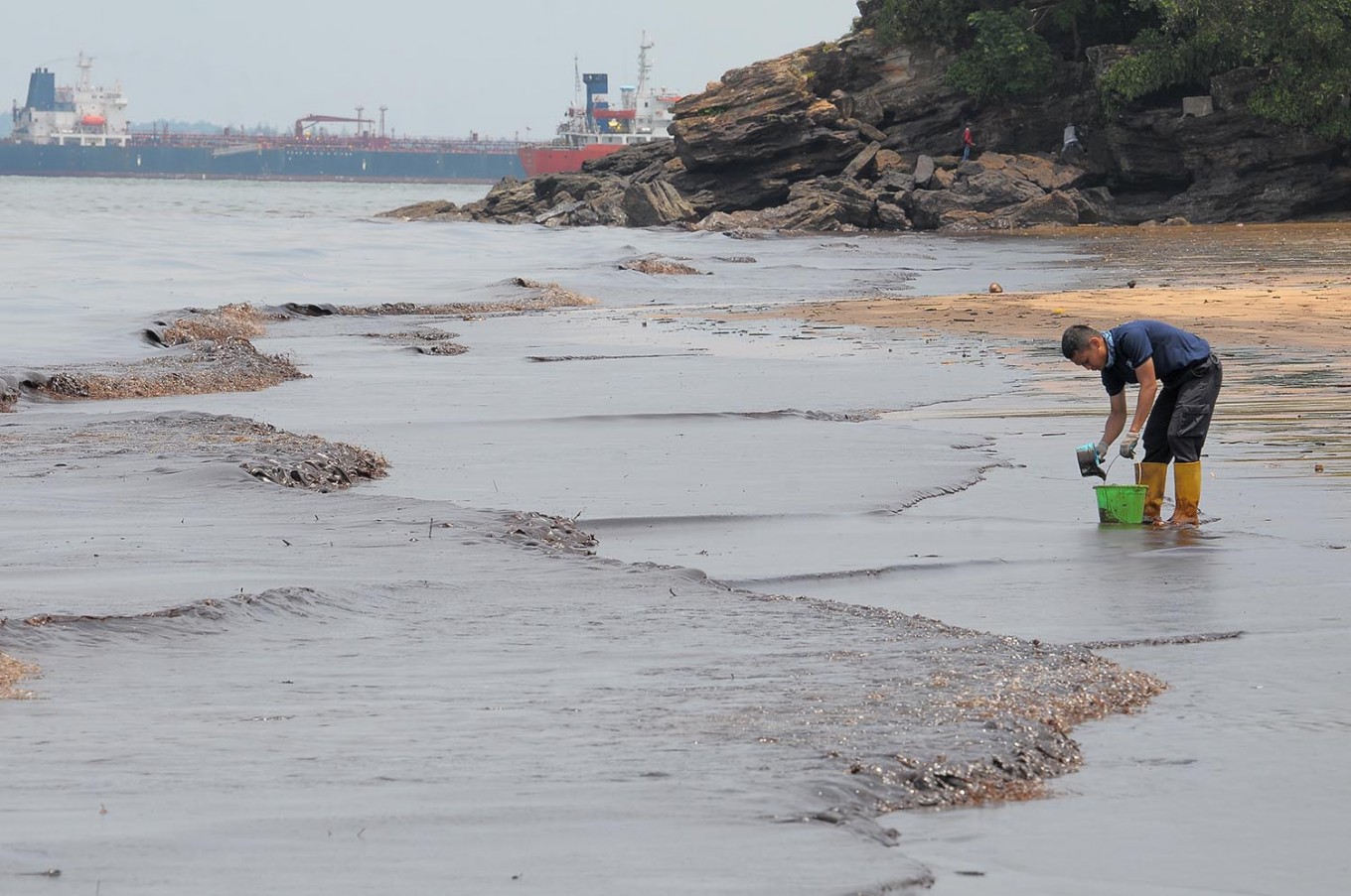 Manual labor: A police officer collects oil by hand on April 2 from the polluted waters off Banua Patra Beach in Balikpapan, East Kalimantan.