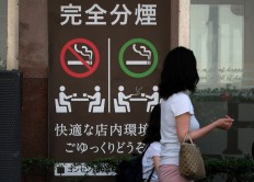 A mother and her daughter walk past a coffee shop displaying a sign saying 'Complete separation of smoking areas: Non-smoking and Smoking' in Tokyo on June 27, 2018.