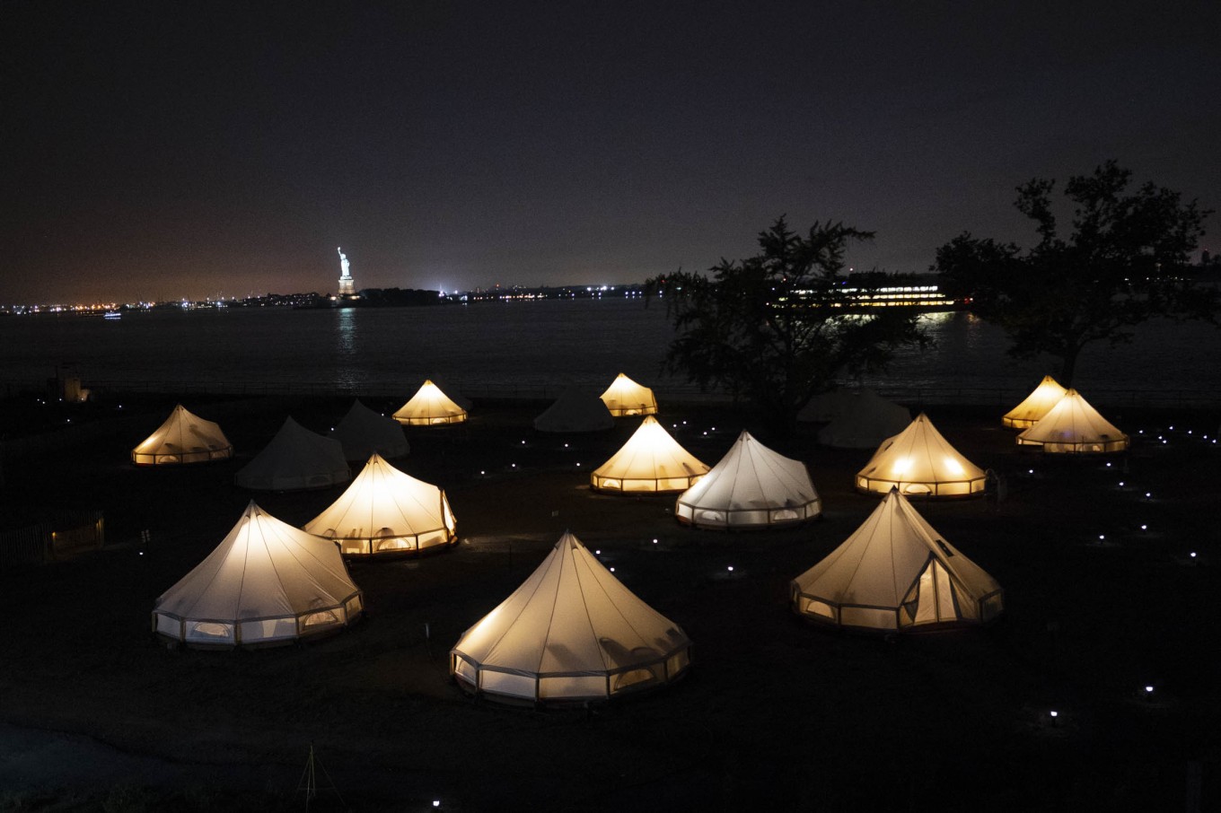 Glowing journey tents at night against the Statue of Liberty and the Staten Island Ferry.