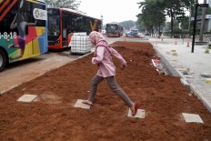 A commuter hops across a footpath to get to a bus in Sudirman, Central Jakarta, on Tuesday, July 24, 2018. In the city administration’s new sidewalk design, a 2.5-meter green space will separate the sidewalk and bus stops. JP/Wendra Ajistyatama