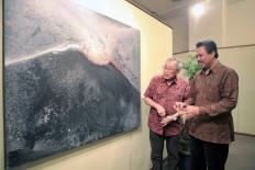 Centre for Strategic and International Studies (CSIS) cofounder Jusuf Wanandi (left) and painter I Wayan Karja look at a painting of a volcano at the artist’s Cosmic Energy exhibition in Jakarta in 2018. CSIS has begun to focus more on climate change and natural disasters, executive director Philips J. Vermonte has said.
