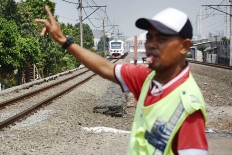 A resident manages traffic at a railway crossing in Rawa Buaya, West Jakarta, on Wednesday, while a train approaches. Some railway crossings in the capital do not have proper barriers and pose a danger to motorists.