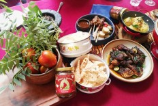 A jar of 'sambal koja' is seen among tomatoes,  'salam koja' (curry leaves), crackers, grilled chicken, satay and boiled eggs in yellow soup.
