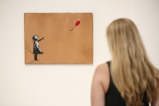 A gallery assistant poses with 'Girl with Balloon' 2006 artwork by Banksy at Lazinc Gallery in London on July 11