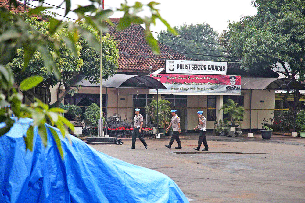 Police officers walk in front of Ciracas Police station in East Jakarta on Dec. 12. A mob destroyed and burned part of the building and a number of vehicles early on Wednesday.