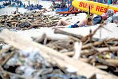 Two tourists sunbathe on Kuta Beach in Bali, where waste is piled up along the shore. 