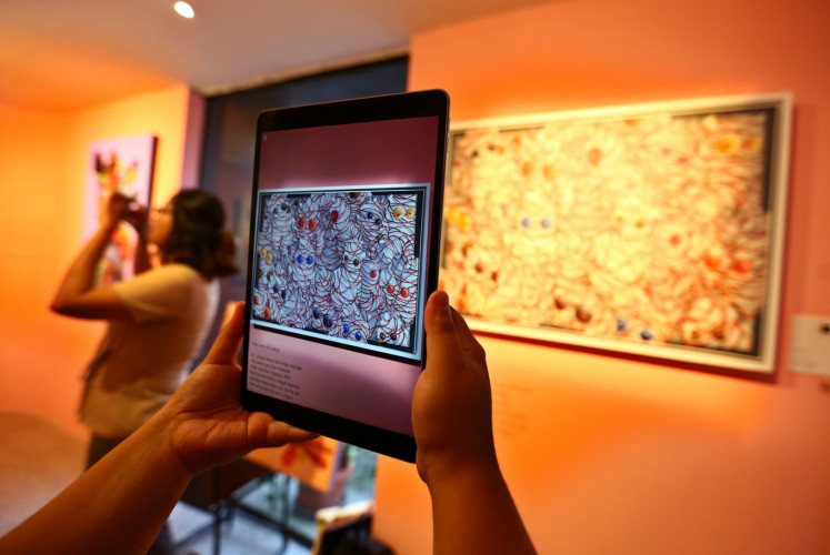 A visitor samples augmented reality (AR) technology in front of Kencut's 'Kepenuhan' (full) painting at 'Kaum Mata Kancing' exhibition by I Putu Adi 'Kencut' Suanjaya on Friday, Jan. 18 at Kopi Kalyan, South Jakarta.
