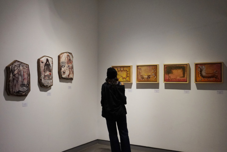 A visitor stands between artworks by Ngakan Putu Agus Arta Wijaya (right) and Ruth Marbun (left).