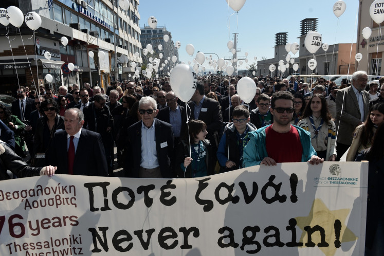 People hold a banner and balloons reading 'Never Again' as they walk towards the old railway station to mark the departure of the first train from Thessaloniki to Auschwitz concentration camp in Poland on March 15, 1943, during a silent march in memory of Holocaust victims in Thessaloniki, on March 17, 2019.