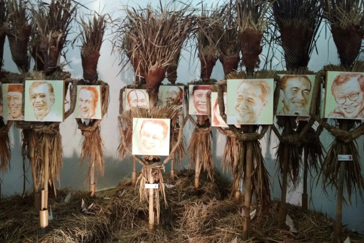 Scarecrows hold portraits of Indonesian politicians showing joyous expressions in Hari Budiono's 'Memedi Sawah' exhibition.