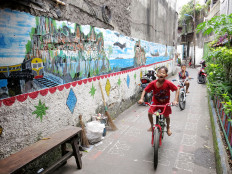 Children ride their bicycles in a narrow alley near Jl. Palmerah Barat, West Jakarta, on Monday. Local residents have organized a local project to beautify their alleyway with plants and murals.
