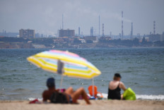 In this file photo taken on June 21, 2017 people enjoy the sun at a beach in Fos-sur-Mer, southern France, as fumes rise from the chimneys of a refinery plant in the background.