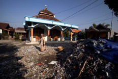An elderly woman is sundrying waste in front of her house and the nearby mosque. JP/Sigit Pamungkas