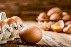 Eggs in a carton box and a broken egg with yolk in background