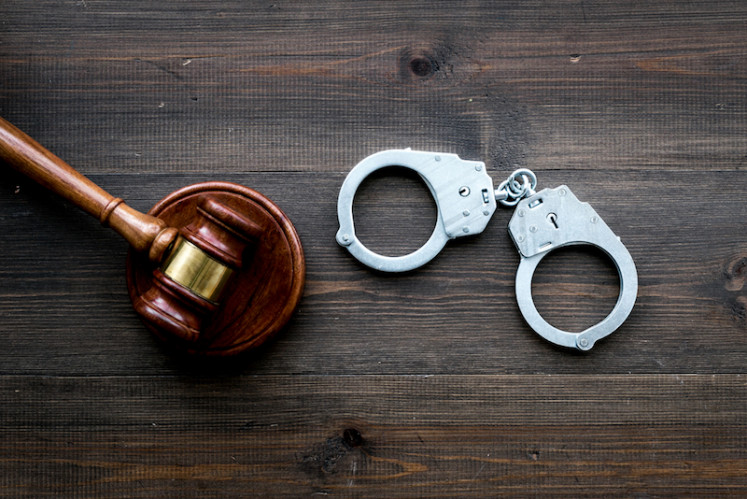 Metal handcuffs near judge gavel on dark wooden background