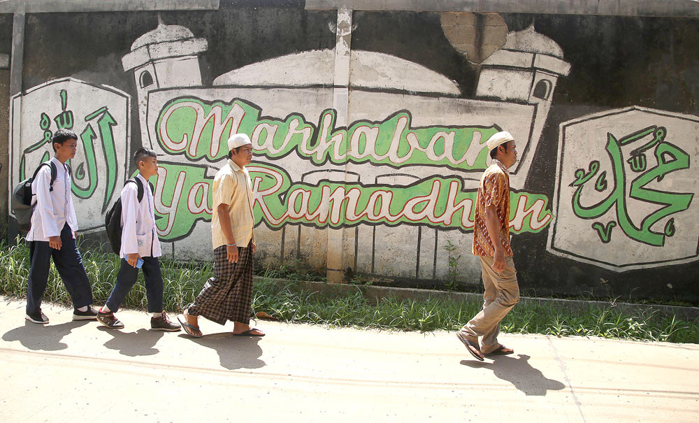 People walk past a mural that reads "Marhaban ya Ramadhan" (Welcome Ramadan) on their way to a mosque for Friday prayers.