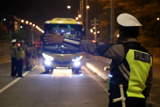 A policeman stops a bus at the gate of Suramadu bridge connecting Madura island and Java island in Surabaya, East Java, on Sunday. The joint security personnel in several regions in the country have raided bus terminals and stations to prevent people from participating in the planned rally to reject election results initiated by supporters of losing candidate Prabowo Subianto. 