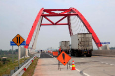 Drive slow: Trucks drive on the Kalikuto Bridge as construction workers in the distance resurface a toll road to ensure passengers enjoy a safe travel experience in Batang regency, Central Java, on Monday. JP/Suherdjoko