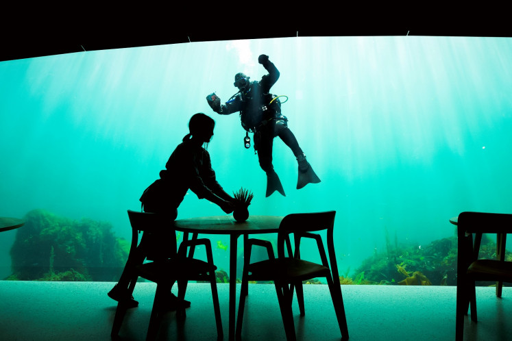 A worker prepares the dining tables as a diver cleans the outside of a viewing window of Under, a restaurant that is semi-submerged beneath the waters of the North Sea on May 2, 2019 in Lindesnes near Kristiansand, some 400 km south west of Oslo. 