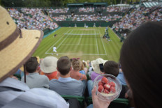 A spectator eats strawberries and cream as she watches Spain's David Ferrer play against Russia's Andrey Kuznetsov during their men's singles second round match on day three of the 2014 Wimbledon Championships at The All England Tennis Club in Wimbledon, southwest London, on June 25, 2014