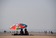 Beach-goers shelter under an umbrella by the sea in Camber Sands, southern England on July 25, 2019, during a heatwave in Britain. 