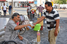 A customer buys a glass of legmi from a street vendor, a coveted date palm drink, in the southwestern Tunisian town of Gabes on July 18, 2019. 