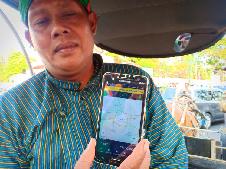 Riyanto, a horse-drawn carriage driver shows the GrabAndong app on his smartphone on Aug. 24.