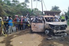 Police officials examine a burned car in Cidahu, Sukabumi, West Java as local residents look on. Police arrested six people related to the murder of a father and son whose bodies were found inside the car. 
