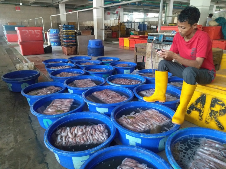 A vendor looks at mobile phone while waiting for frozen squid to defrost in Muara Baru Modern Fish Market in Penjaringan, North Jakarta on Saturday, Sept 14 2019.