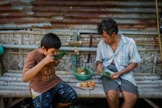 Rizki enjoys traditional snacks with his grandfather, Suyatiman, in the side yard of the house. JP/ Anggertimur Lanang Tinarbuko