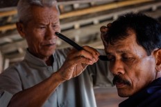 Suhardi focuses on the hair around the ear of a customer. JP/Anggertimur Lanang Tinarbuko